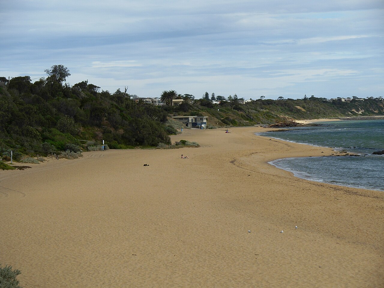 A quiet day at Sandringham Beach, with sand curving towards the cliffs