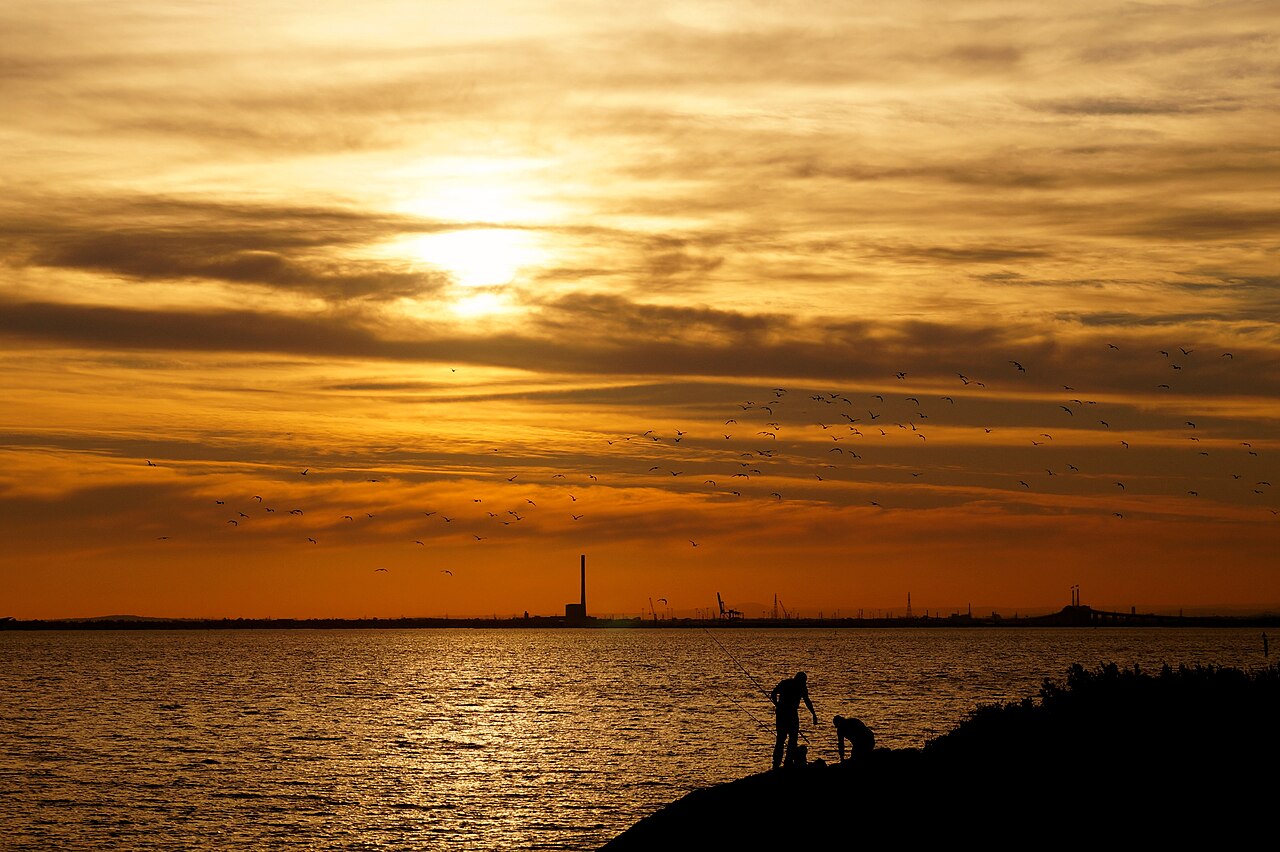 Fishermen silhouetted against an orange sunset over the bay in St Kilda