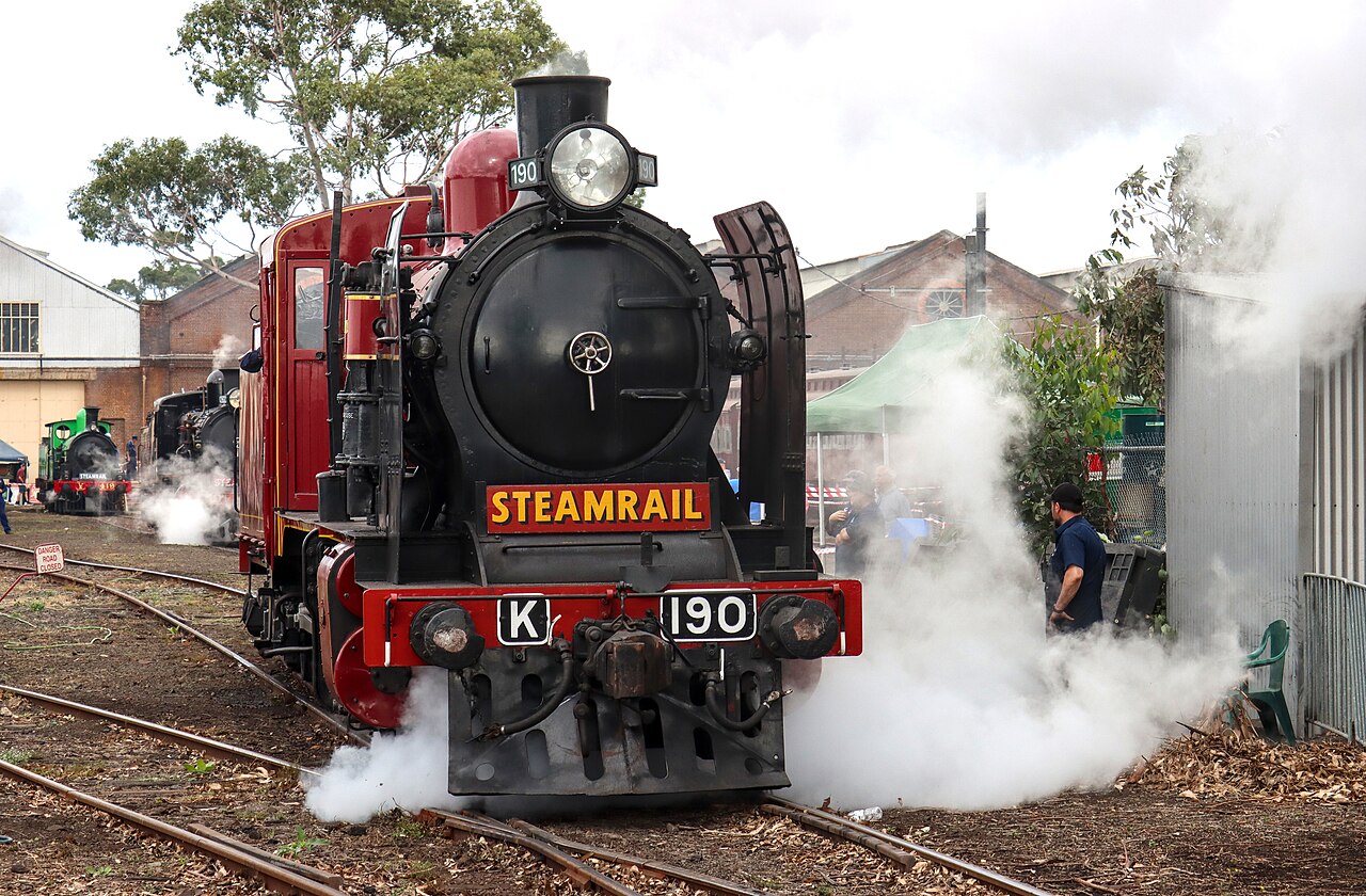 Steam locomotive K 190 surrounded by steam beside workshop buildings