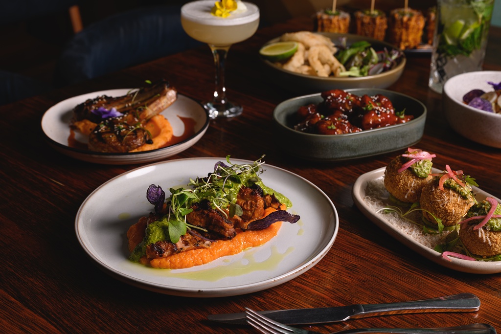 A generous ONDA spread — lamb chops on terracotta-orange puree, chicken under bright green sauce with violet sweet-potato crisps, sticky red-glazed wings, calamari and salad, golden arancini with pesto, mojito and that signature egg-white cocktail.